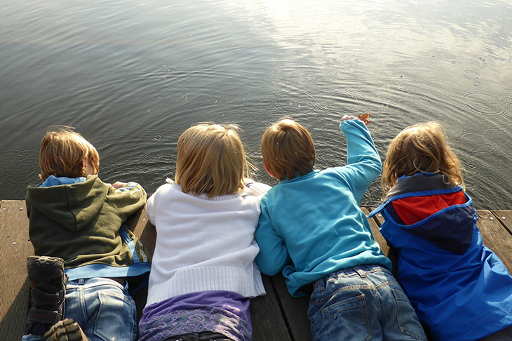 Fyra barn som ligger på mage på en brygga och tittar ner i vattnet.