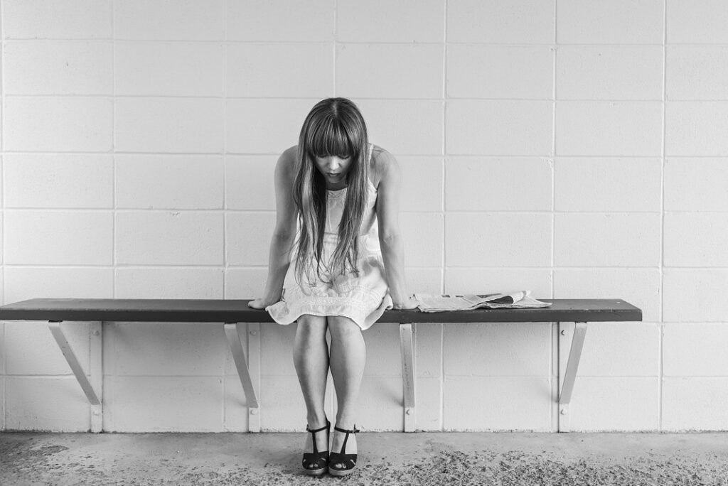 Flicka som sitter själv på en bänk och tittar ner i marken.